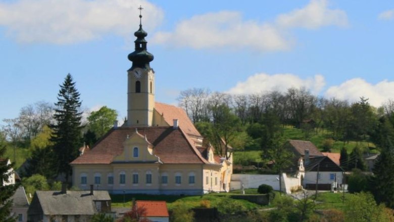 Obersulz, © Kling Kirche mit Turm in ländlicher Umgebung, umgeben von Bäumen und Häusern.