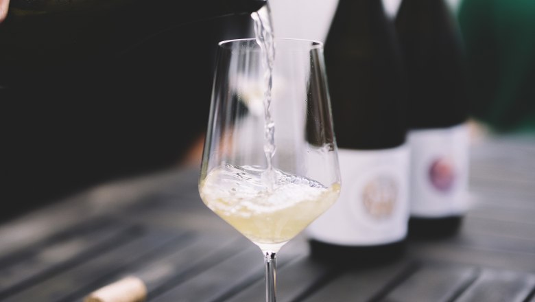 Wein einschenken, © Niederösterreich Werbung / Mara Hohla Weißwein wird in ein Glas auf einem Tisch eingeschenkt.