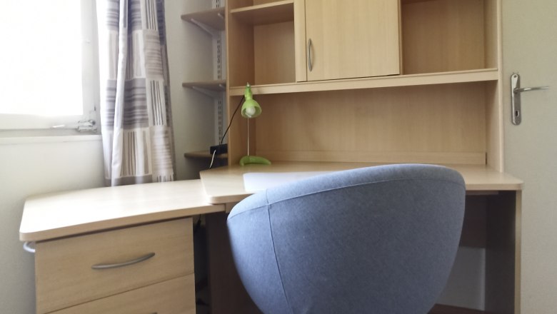 Writing desk, © Multimedia Lauda A modern desk with a gray office chair and a shelf with drawers and compartments.