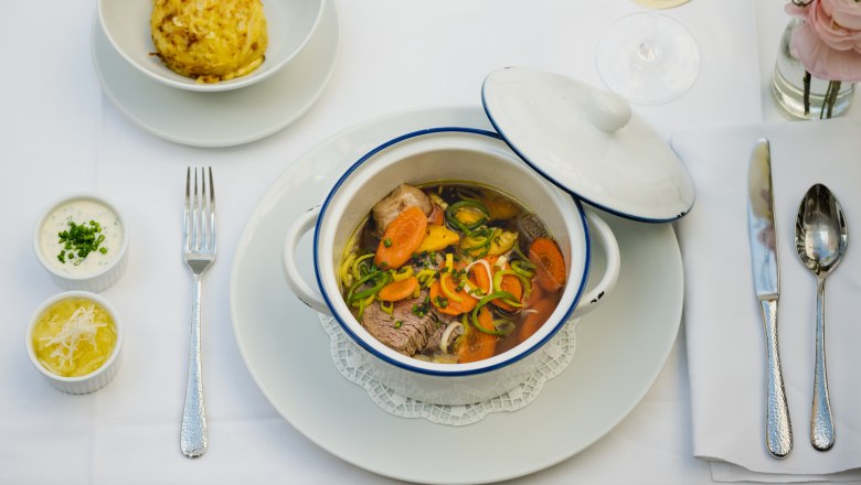 Herzlich Willkommen, © NÖ Werbung / Martina Siebenhandl Ein gedeckter Tisch mit einem Eintopf in einem weißen Topf, einem Knödel, zwei Soßen und einem Glas Weißwein.