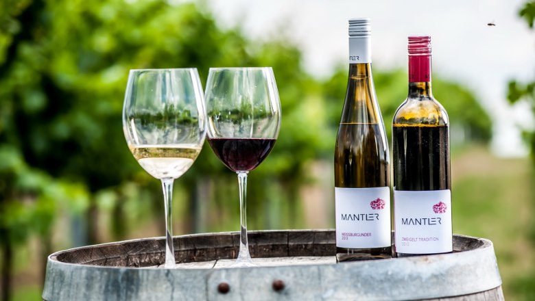 Mantler Weine, © Weingut Mantler Zwei Weingläser und zwei Weinflaschen auf einem Fass im Weinberg.