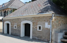 Kellergasse Langenzersdorf, © Weinviertel Tourismus Ein traditionelles Gebäude mit Steinmauer und Schieferdach in Langenzersdorf.