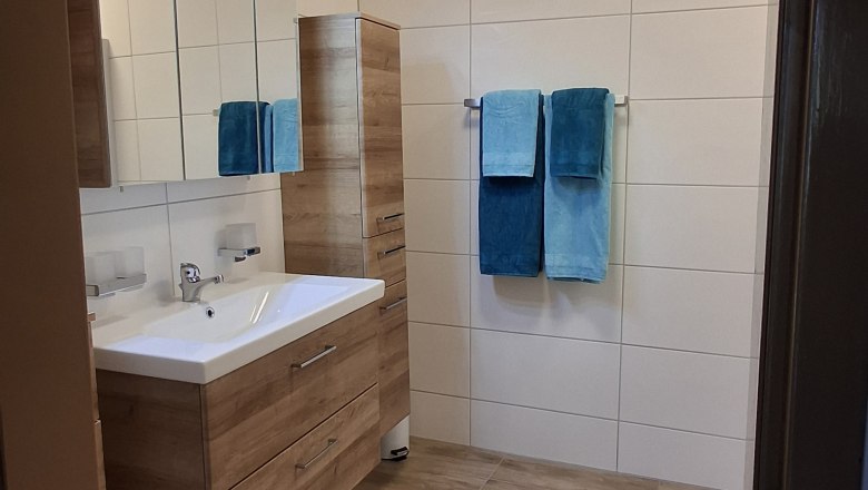 Badezimmer, © Fam. Teufelsbauer Modernes Badezimmer mit Holzdecke, Waschtisch, Spiegel, Handtüchern und Teppich.