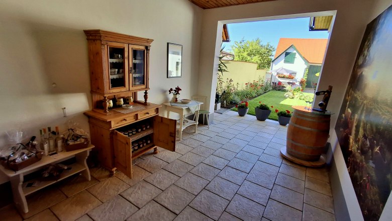 Eingangsbereich, © Fam. Teufelsbauer Eingangsbereich mit Holzmöbeln, Pflanzen und Blick auf einen Garten.