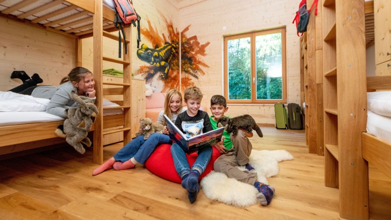 Wildkatzen Camp, © Waldviertel Tourismus / Studio Kerschbaum Kinder in einem Holzzimmer mit Etagenbetten, lesen ein Buch und halten Plüschtiere.