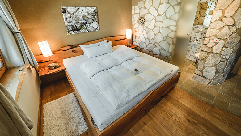 Stone room, © Matthias Auer Cozy bedroom with wooden bed, stone walls and modern bathroom.
