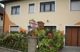 Hausansicht, © Fam. Völker Haus mit gelber Fassade, Blumendekoration und Schild 'Zimmer'.