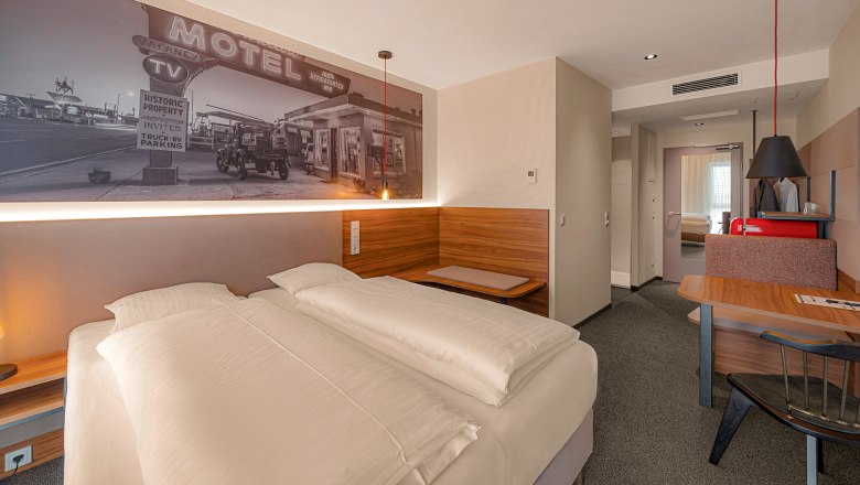 Zündwerk Motel, © propertyphotos.at Modernes Hotelzimmer mit Doppelbett, Wandbild eines alten Motels, Holzmöbeln und Schreibtisch.