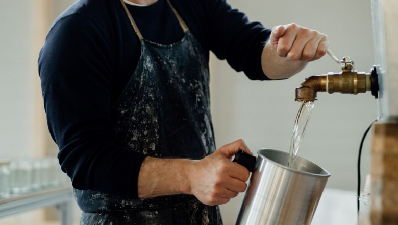 Kerzenmanufaktur, © Glaser Kerzen Person füllt Wasser aus einem Hahn in einen Metallbehälter.