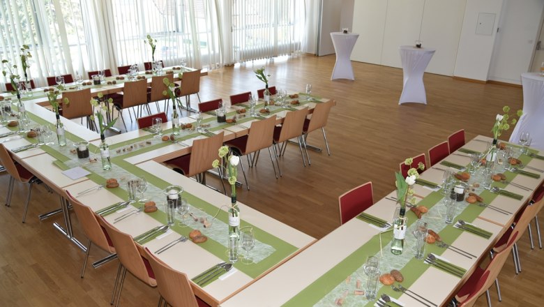 Ballroom, © Restaurant Hacker's A festively decorated hall with tables arranged in a U-shape, green table runners and floral decorations.