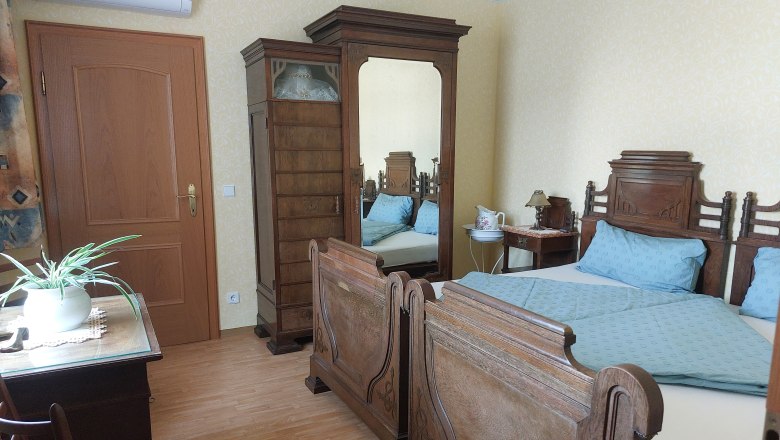 Bedroom, © Erika Kellner Bedroom with antique wooden furniture, double bed, wardrobe with mirror, table with plant and chair.