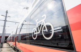 Zug, © Weinviertel Tourismus GmbH / Herbst Nahaufnahme eines modernen Zuges mit einem Fahrradsymbol auf dem Fenster, das auf Fahrradmitnahme hinweist.