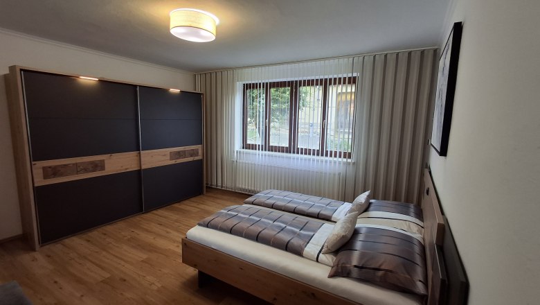 Schlafzimmer, © Fam. Teufelsbauer Modernes Schlafzimmer mit Doppelbett, großem Kleiderschrank und Fenster mit Jalousien.