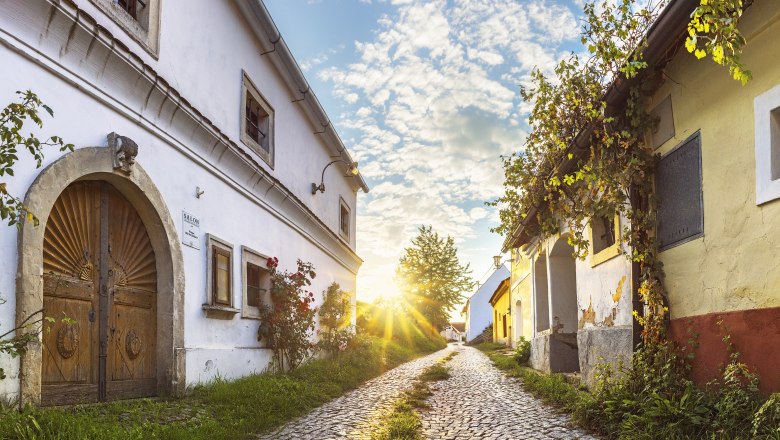 Wine cellar lane in Röschitz, © Reinhard Podolsky Cobblestone street in Röschitz with historic buildings and sunset.