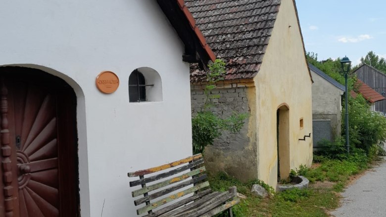 Wine cellar lane Niederleis, © Weinviertel Tourismus A row of small, traditional buildings with tiled roofs and a wooden bench in front of them.