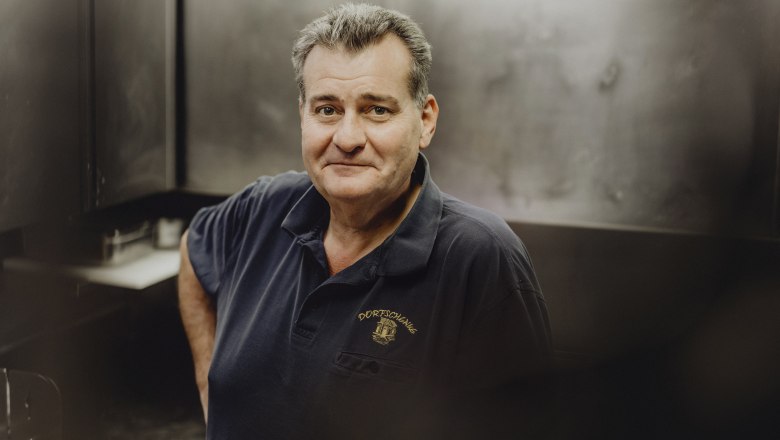 Landlord Horst Bischof, © Niederösterreich Werbung/Sophie Menegaldo Man in a dark polo shirt with the "Dorfschenke" logo in a kitchen.