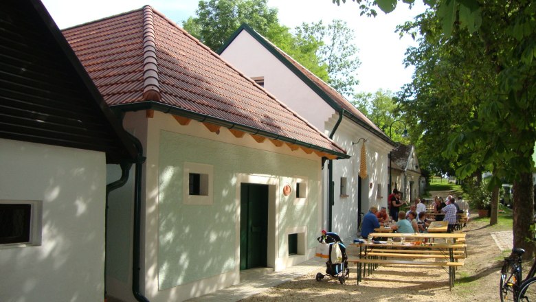 Wine cellar lane in Asparn/Zaya, © Sarer People sit at tables in front of traditional buildings with red roofs.