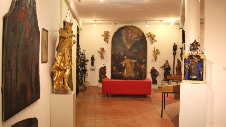 Belvedereschlössl/Bezirksmuseum Stockerau, © Stadtgemeinde Stockerau Innenansicht eines Museums mit Skulpturen und Gemälden, rotes Sofa in der Mitte.