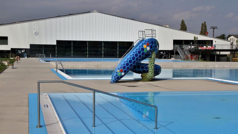 Florian Berndl Bathroom, © Marktgemeinde Bisamberg An empty outdoor pool with a colorful slide and a large building in the background.