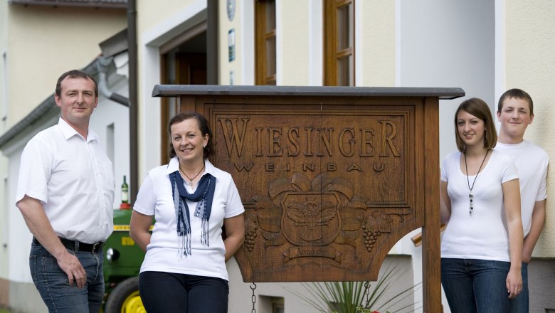 Familie Wiesinger, © Michael Himml Vier Personen stehen vor einem Schild mit der Aufschrift 'Wiesinger Weinbau'.
