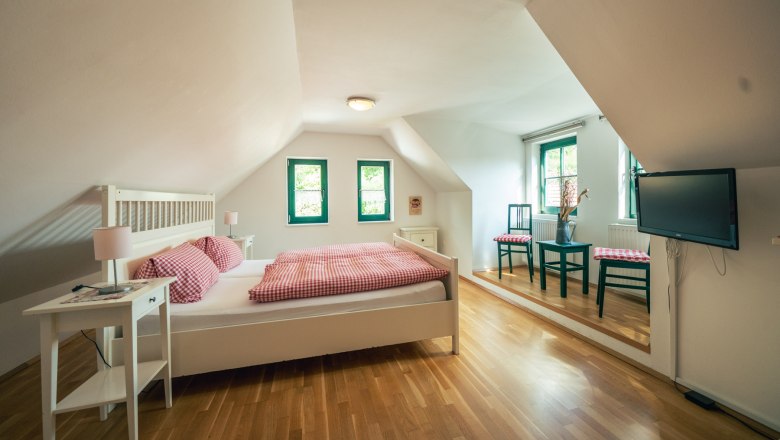 Winzerhof Küssler, © Winzerhof Küssler Gemütliches Schlafzimmer mit Holzboden, Doppelbett, Nachttischen, zwei Stühlen und einem Fernseher an der Wand.