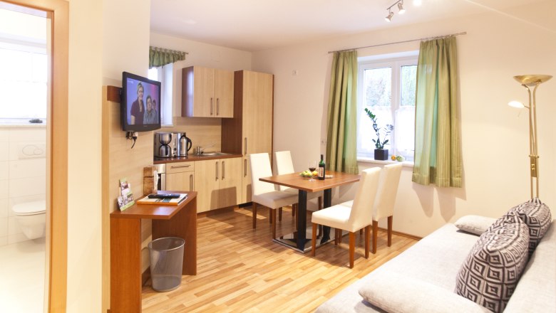 Kitchen and lounge area, © Astrid Bartl Modern kitchen with dining table, sofa and TV in a bright room.