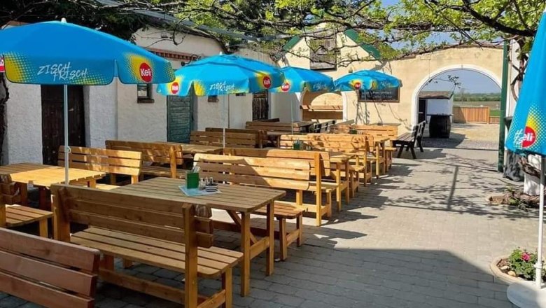 Gastgarten, © Hanfwirt Ein sonniger Gastgarten mit Holzbänken und blauen Sonnenschirmen.