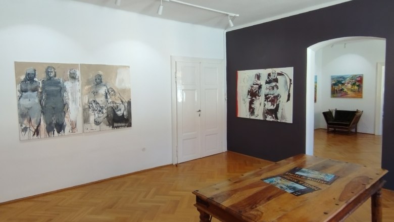 the MERKIMA Gallery, © Doris Hauser Interior view of an art gallery with wooden floor, paintings on the walls and a wooden table in the middle.