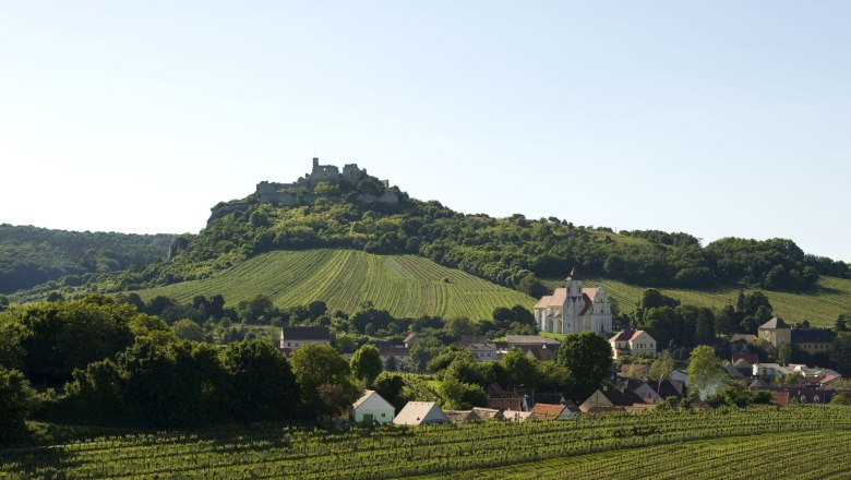 Burgruine Falkenstein, © Michael Himml Landschaft mit Burg auf einem Hügel, Weinberge und Dorf im Vordergrund.