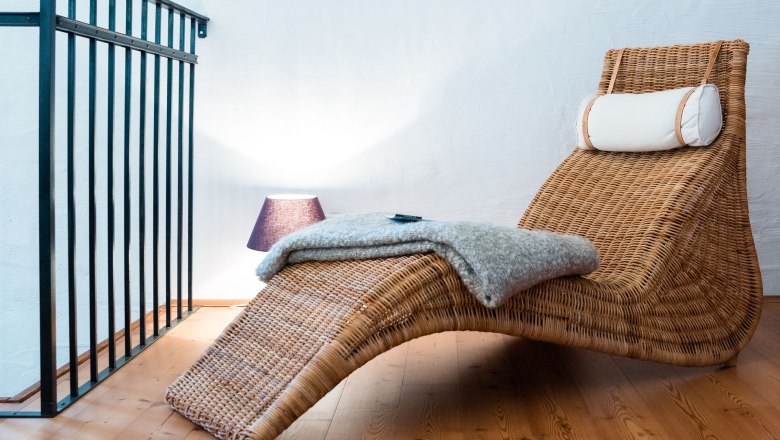 Leseecke, © Weinakademie Retz Eine gemütliche Leseecke mit einem geflochtenen Liegestuhl, einer Decke und einer Lampe auf Holzboden.