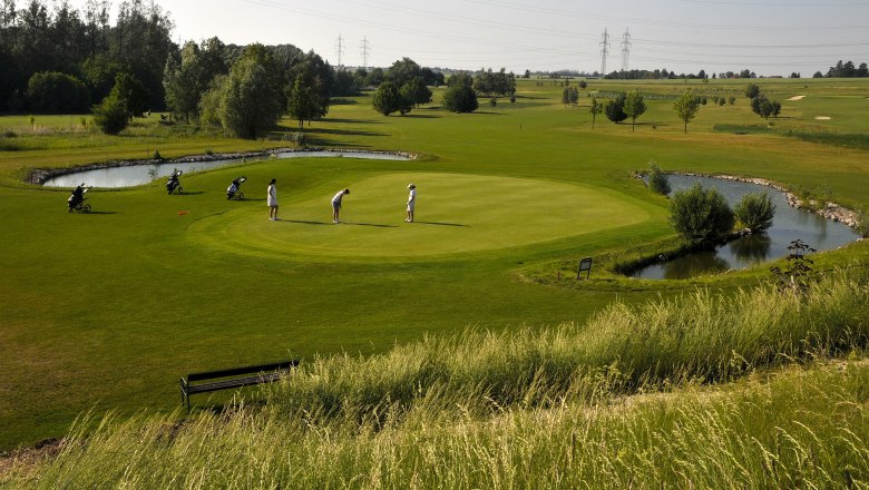 Golfplatz Spillern, © Weinviertel Tourismus / Mandl Golfer auf einem grünen Golfplatz mit Teich und Bäumen im Hintergrund.