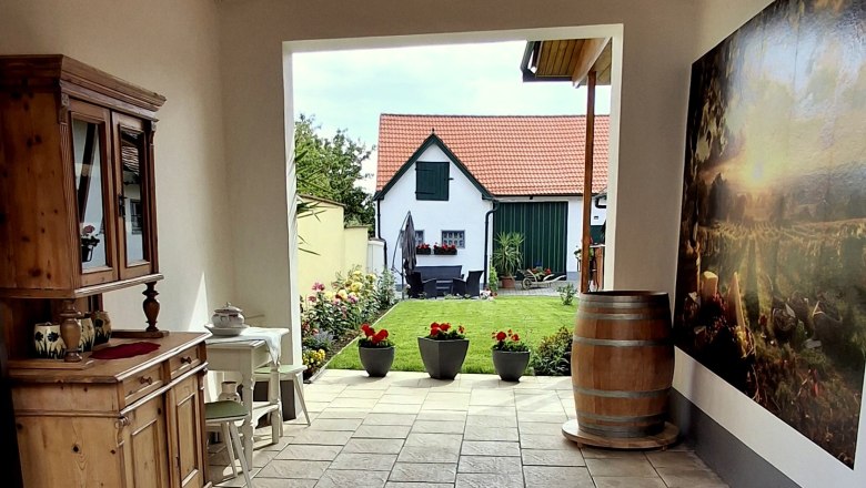Blick auf den Innenhof, © Fam. Teufelsbauer Innenhof mit Holzmöbeln, Pflanzen und Blick auf ein Haus mit rotem Dach.