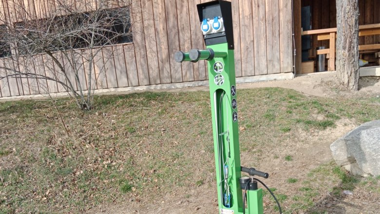 E-Bike-Ladestation, © Stadtgemeinde Maissau Grüne E-Bike-Ladestation vor einem Holzgebäude.