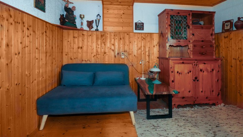Zusatzbett im Stüberl, © Novasol / Fam. Schachner Gemütliches Zimmer mit Holzwänden, einem blauen Sofa, einem Holztisch und einem rustikalen Schrank.
