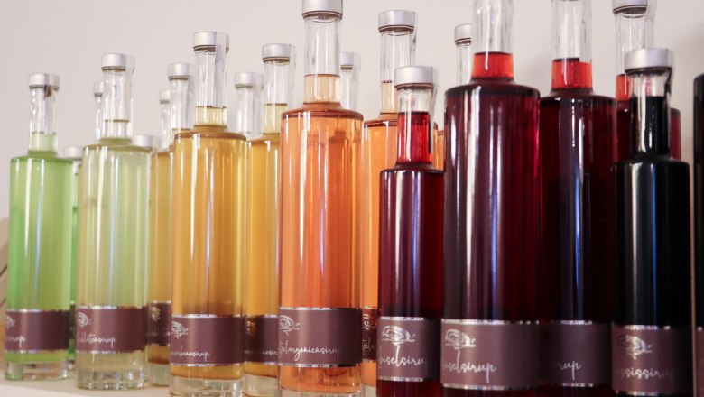 Beerenhof Prenner, © Trixi Rollin Verschiedene bunte Sirupflaschen in einer Reihe auf einem Regal.