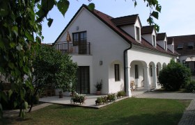 Gästezimmer Parth, © Erika und Hermann Parth Ein weißes Gebäude mit roten Dachziegeln und Arkaden, umgeben von einem Garten mit Bäumen und Blumen.