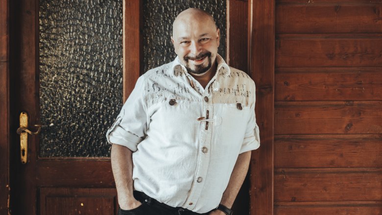 Wirt Franz Burgstaller, © Niederösterreich Werbung/David Schreiber Ein Mann in einem weißen Hemd lehnt lächelnd an einer Holzwand.