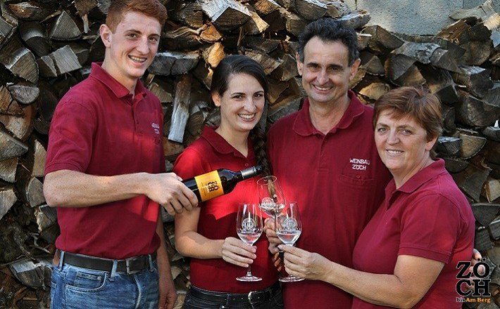 Familie Zöch, © Fam. Zöch Vier Personen in roten Hemden stoßen mit Weingläsern an, vor einem Stapel Holzscheite.