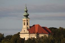 Pfarrkirche St. Nikolaus, Wolfpassing, © Gemeinde Hochleithen Pfarrkirche St. Nikolaus in Wolfpassing mit rotem Dach und grünem Turm vor bewölktem Himmel.