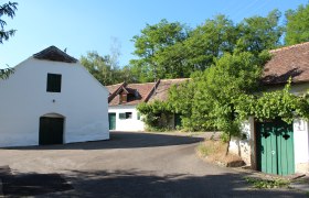 Untermarkersdorf Kellergasse, © Weinviertel Tourismus Traditionelle Weinkeller in einer ländlichen Umgebung mit Bäumen und blauem Himmel.
