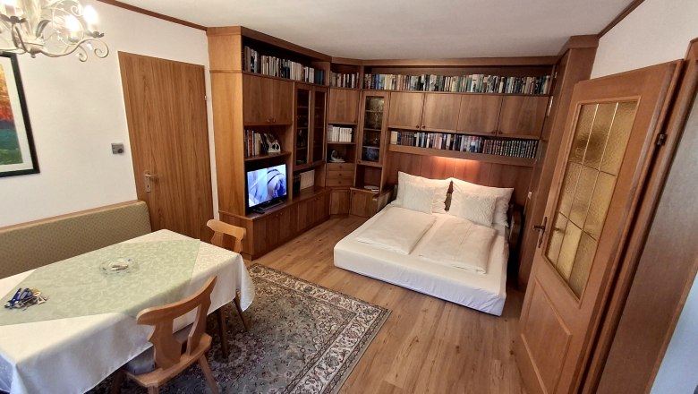 Ausziehcouch, © Fam. Teufelsbauer Wohnzimmer mit ausziehbarer Couch, Bücherregal, Esstisch und Fernseher.