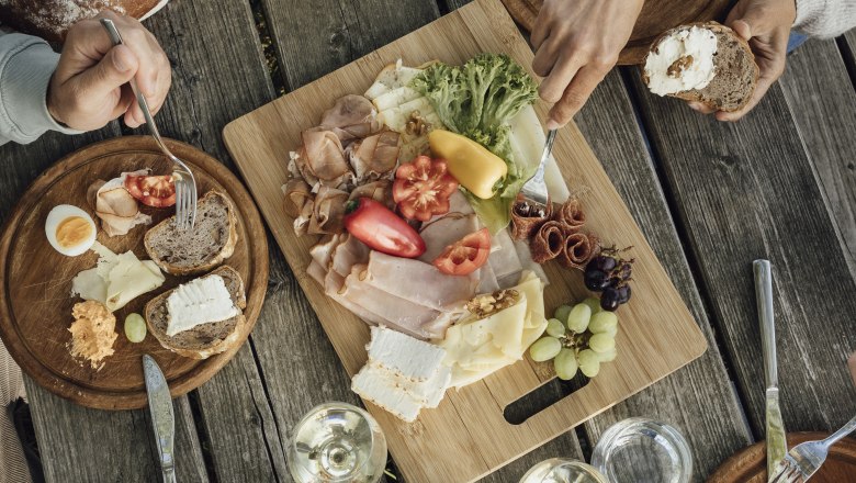 Heurigenjause, © Weinviertel Tourismus GmbH / Sophie Menegaldo Ein rustikaler Holztisch mit einer Jause aus Brot, Käse, Aufschnitt, Gemüse und Wein.