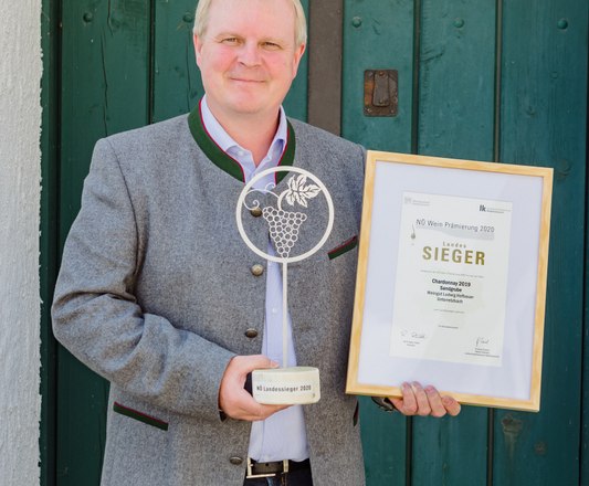 Hofbauer Winery, © Leonardo Ramirez Person holding an award and a certificate in front of a green wooden door.