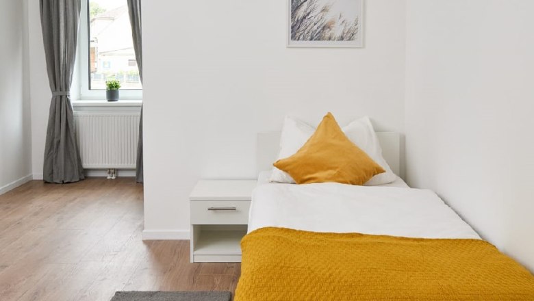 Einzelzimmer, © Eugenia Husti Einzelzimmer mit Bett, Nachttisch und Fenster mit Vorhängen.