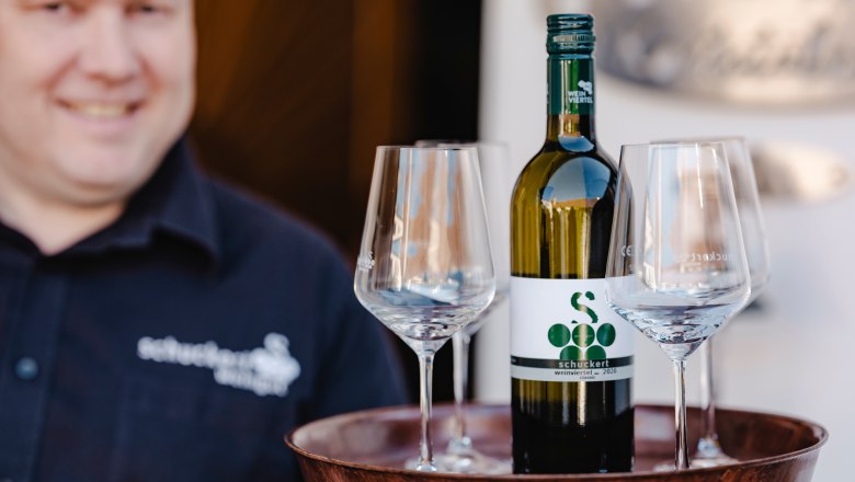 Rainer Schuckert, © Michael Reidinger Ein Mann hält ein Tablett mit einer Weinflasche und drei Gläsern.