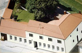 Weinbau Huber, © Huber Luftaufnahme eines Gebäudekomplexes mit rotem Dach und Innenhof mit Bäumen und Spielplatz.