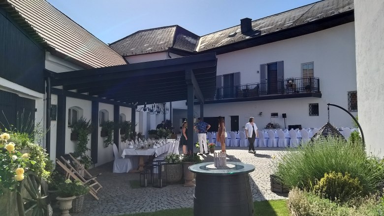 Tafeln im Weinviertel, © Weinviertel Tourismus GmbH Innenhof mit gedeckten Tischen, Blumen und Personen bei sonnigem Wetter.