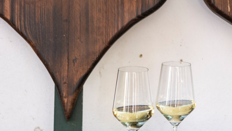 Wine glasses, © Weinviertel Tourismus / Doris Schwarz-König Two wine glasses with white wine on a wooden table in front of a heart-shaped wooden decoration.