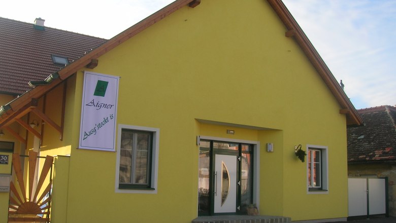 Exterior shot, © Fam Aigner Yellow building with a sign "Aigner Ausg'steckt is" on the façade.
