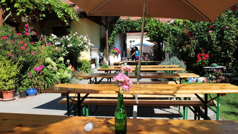Hagenbrunn Wine Days, © Familie Fein A sunny garden with wooden benches, flowers and a parasol.